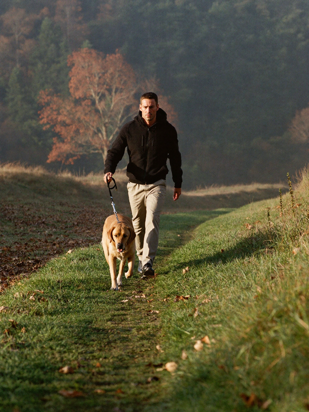 Man in zwarte wafeljack met hond in de duinen