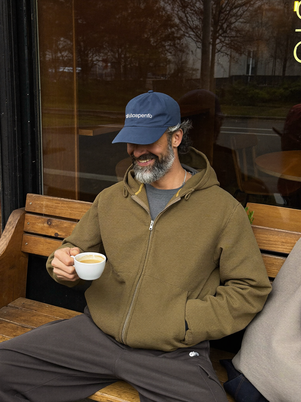 Man in olijfgroene wafeljack met koffie op een terras